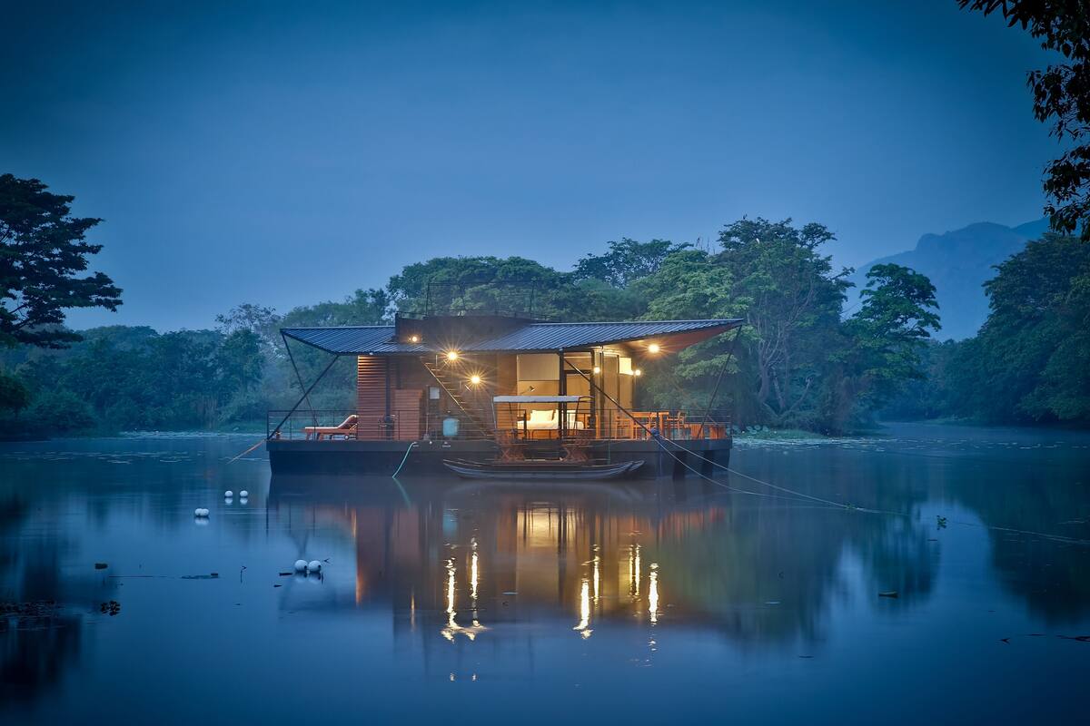 A houseboat with a covered deck, a dining area, and a view of the surrounding water and trees.