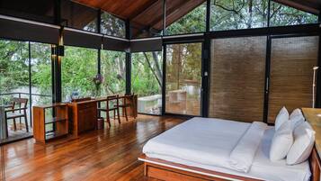 Une chambre à coucher moderne, dotée d’un grand lit, de meubles en bois et offrant une vue sur la forêt grâce à de grandes fenêtres.