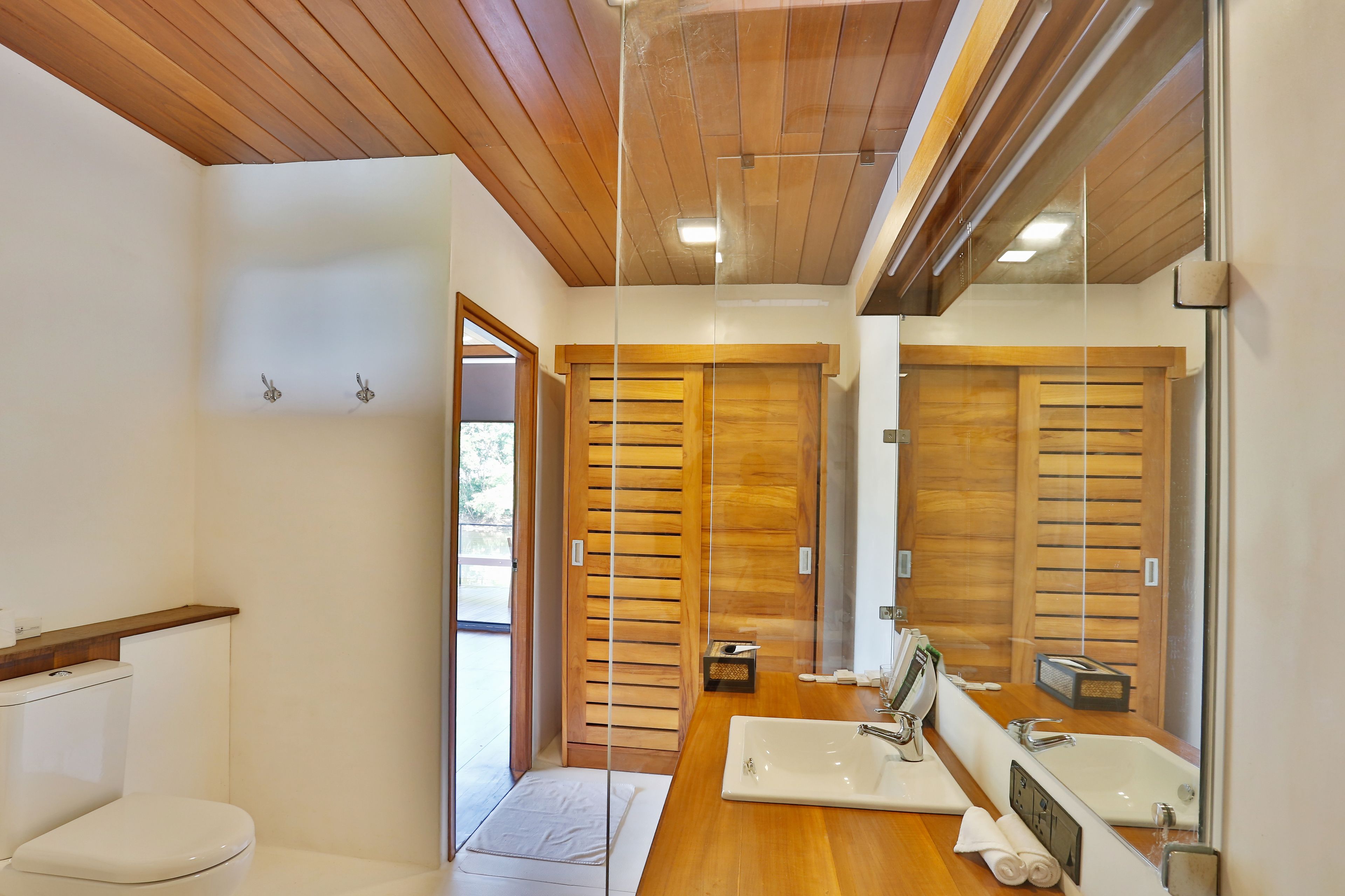 A modern bathroom with wooden ceiling, a large mirror, a wooden vanity, and a toilet.