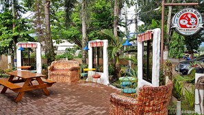 An outdoor seating area with wicker furniture, a wooden table, and a sign for Gabby's Bed & Breakfast. - Gabby's Bed and Breakfast (Dumaguete)