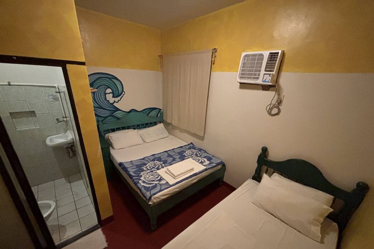Una habitación pequeña con cama individual, ducha, ventana con cortinas y aire acondicionado.
