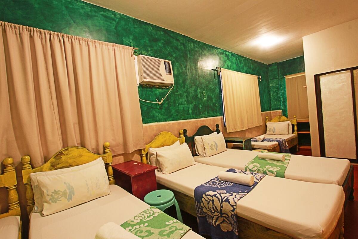Habitación de hotel con dos camas individuales, una mesita, un taburete verde y un armario.