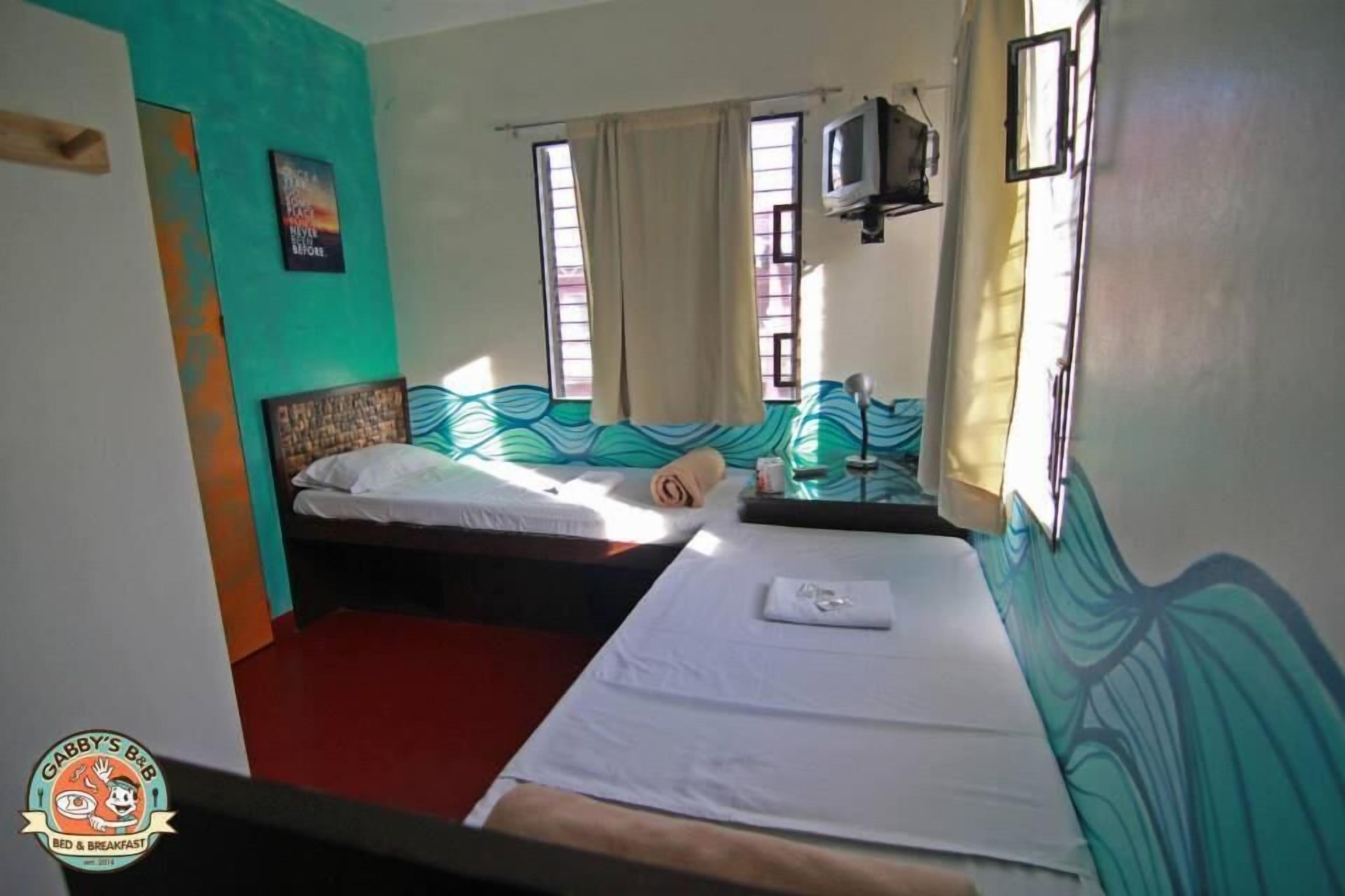 A room with two beds, a window with curtains, a wall with a wave pattern, and a small television.