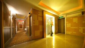 A hotel corridor with a carpeted walkway, a vase with flowers, and a tiled wall. - Ivy Hotel (Ansan)