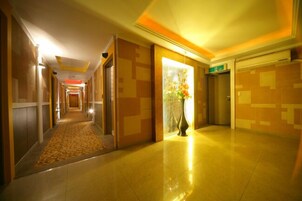 Un pasillo de hotel con un camino alfombrado, un jarrón con flores y una pared de azulejos.