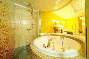 Un baño con una bañera grande, zona de ducha y un espejo sobre una pared amarilla.