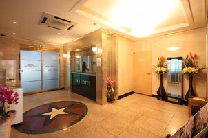 Zona de recepción de un hotel con un diseño de piso en forma de estrella, un mostrador de recepción y una puerta de cristal que da al vestíbulo.