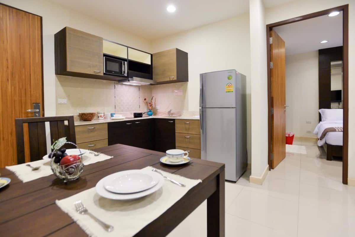 Una cocina moderna con armarios de madera, un refrigerador de acero inoxidable y una zona de comedor con una mesa dispuesta para dos personas.