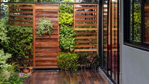 Una valla de madera con diversas plantas, un patio con baldosas y una puerta de cristal.