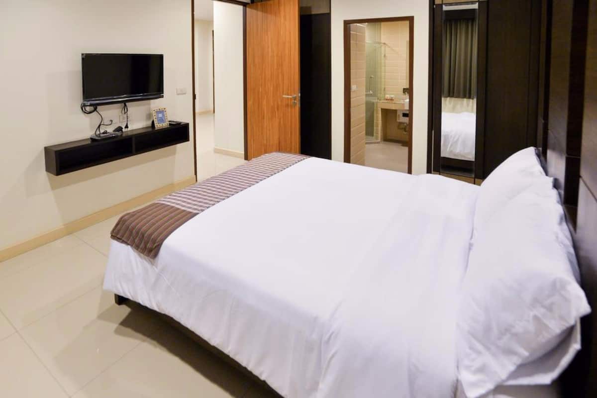 Habitación de hotel con una cama grande, un televisor fijado a la pared, una puerta de madera y un baño a la vista a través de una puerta abierta.