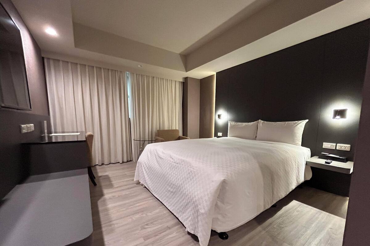 A modern hotel room with a large bed, a desk, and a chair.
