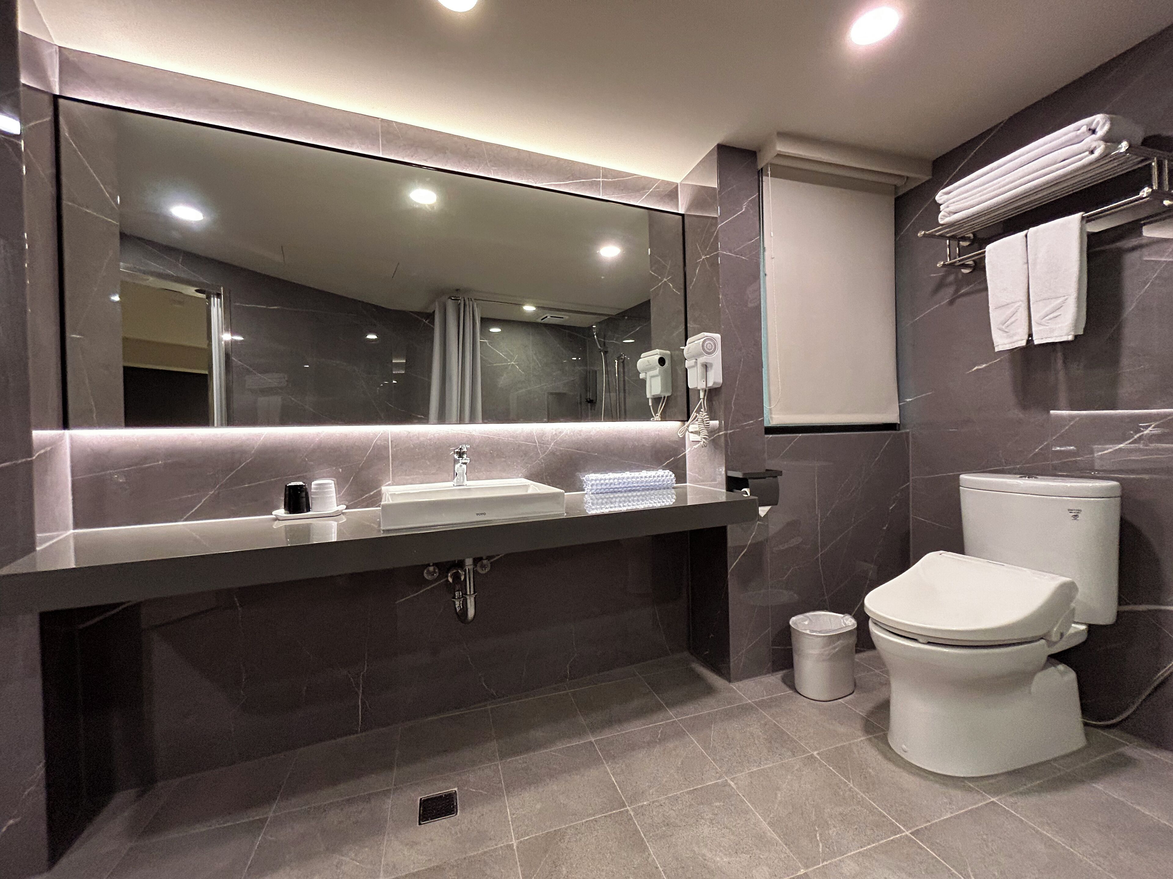 Une salle de bain moderne avec un grand miroir, un lavabo, des toilettes et un porte-serviettes.