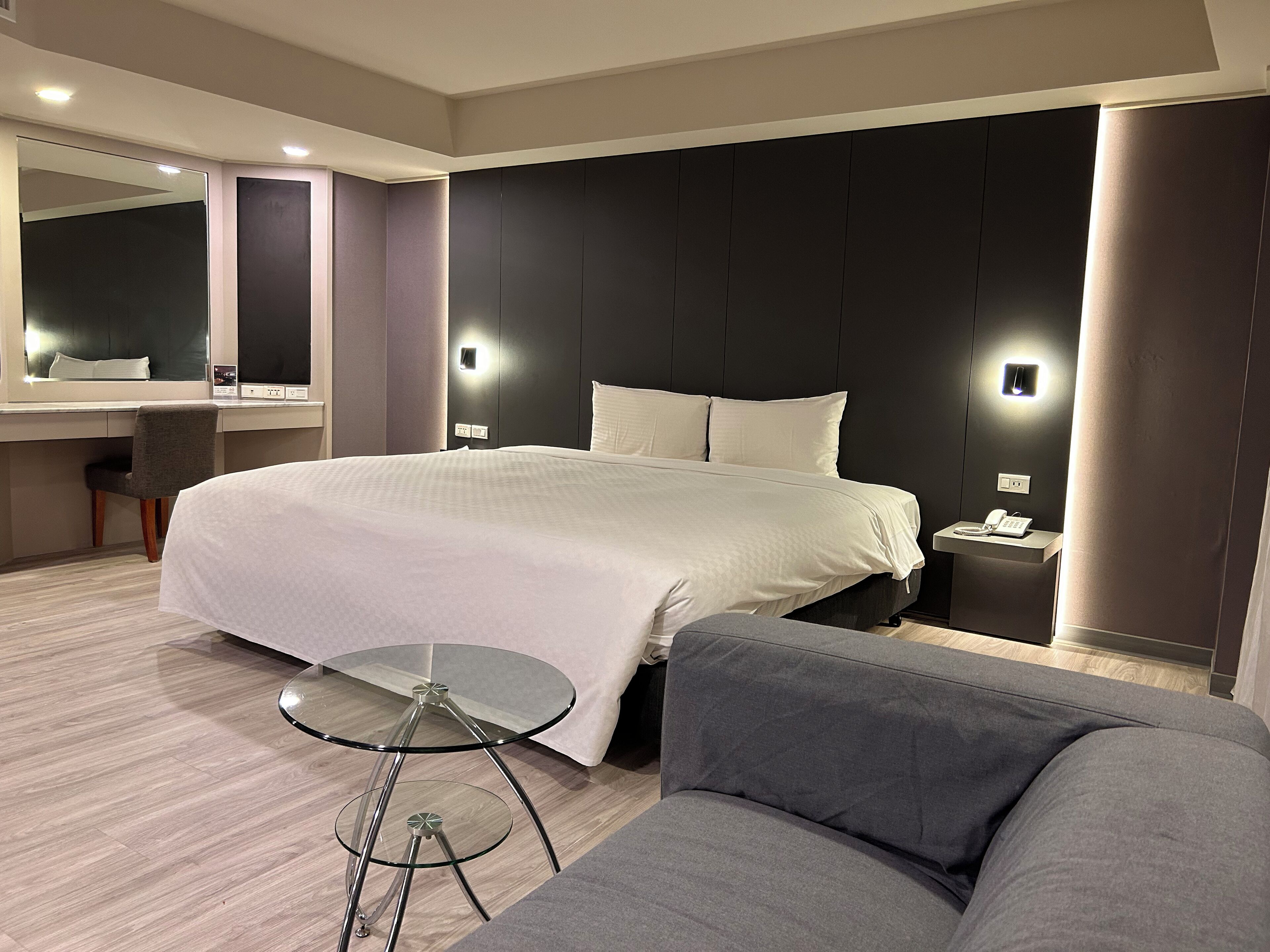 Una habitación de hotel moderna con una cama grande, un escritorio, una silla, una mesita redonda de vidrio y un sofá.