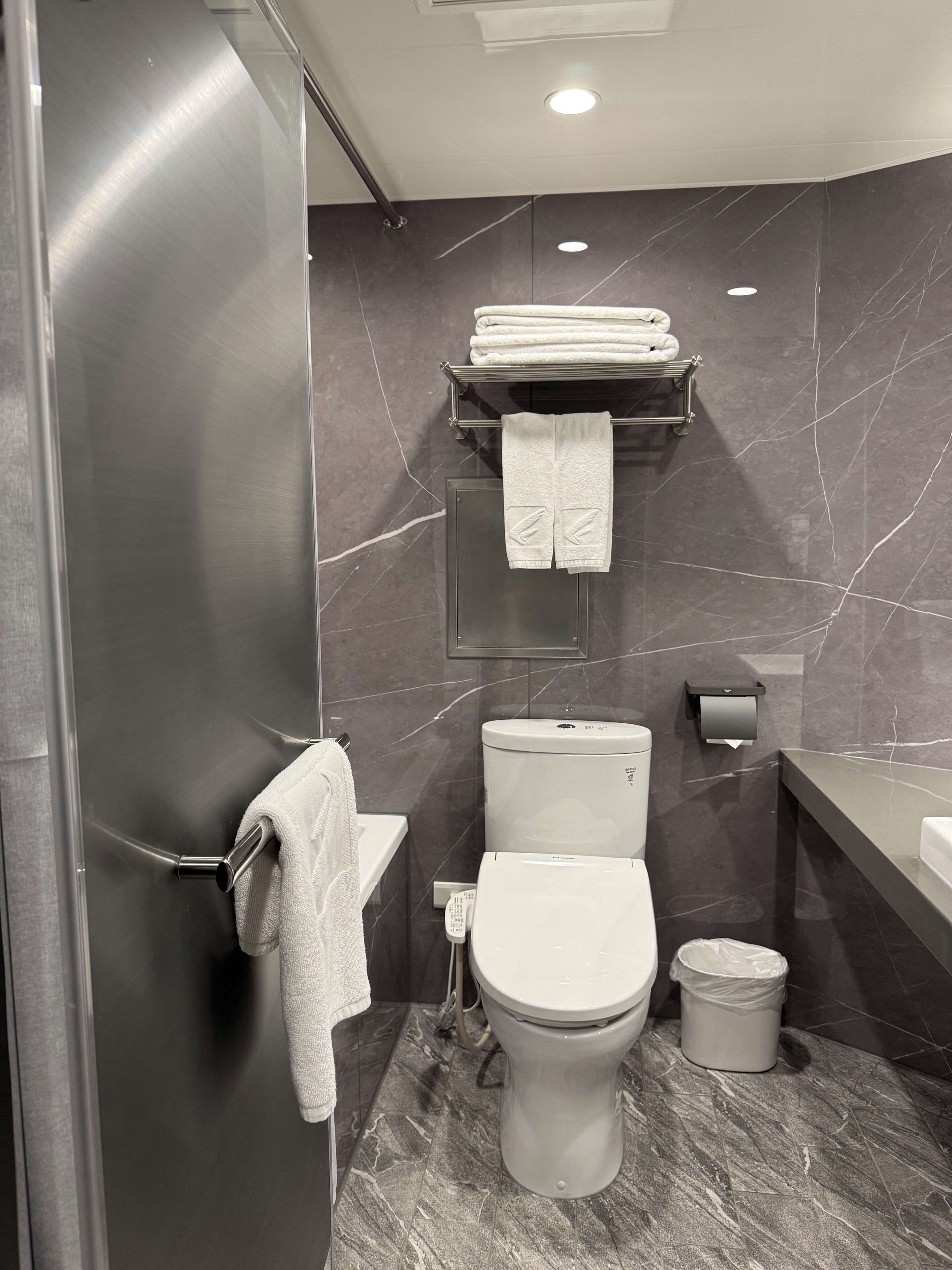 Un baño moderno con inodoro, un bidé, un perchero con toallas dobladas, un cubo de basura y suelo de mármol.