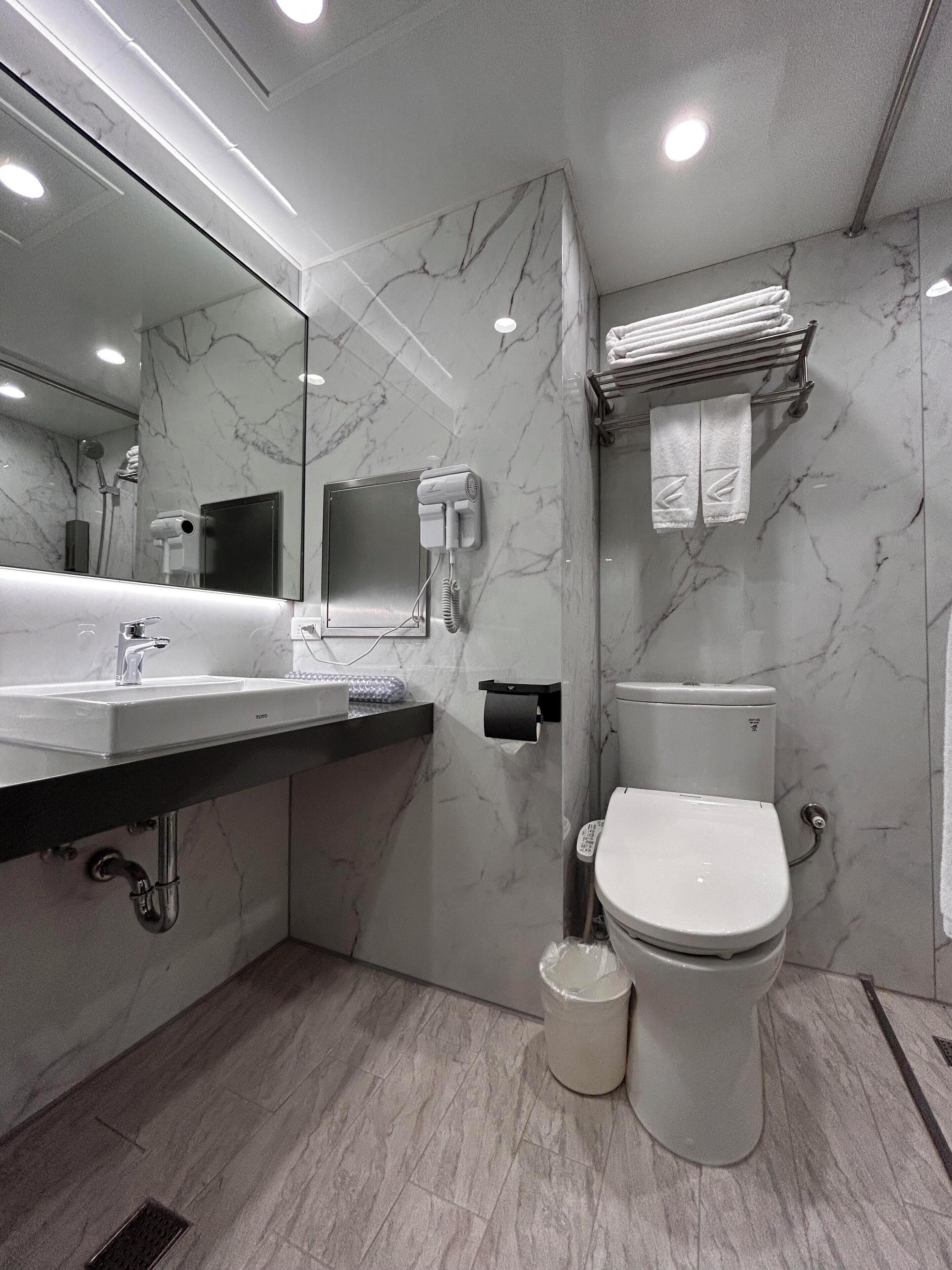 Ein modernes Badezimmer mit Marmorwand, Waschbecken mit Spiegel, Toilette und Handtuchhalter.