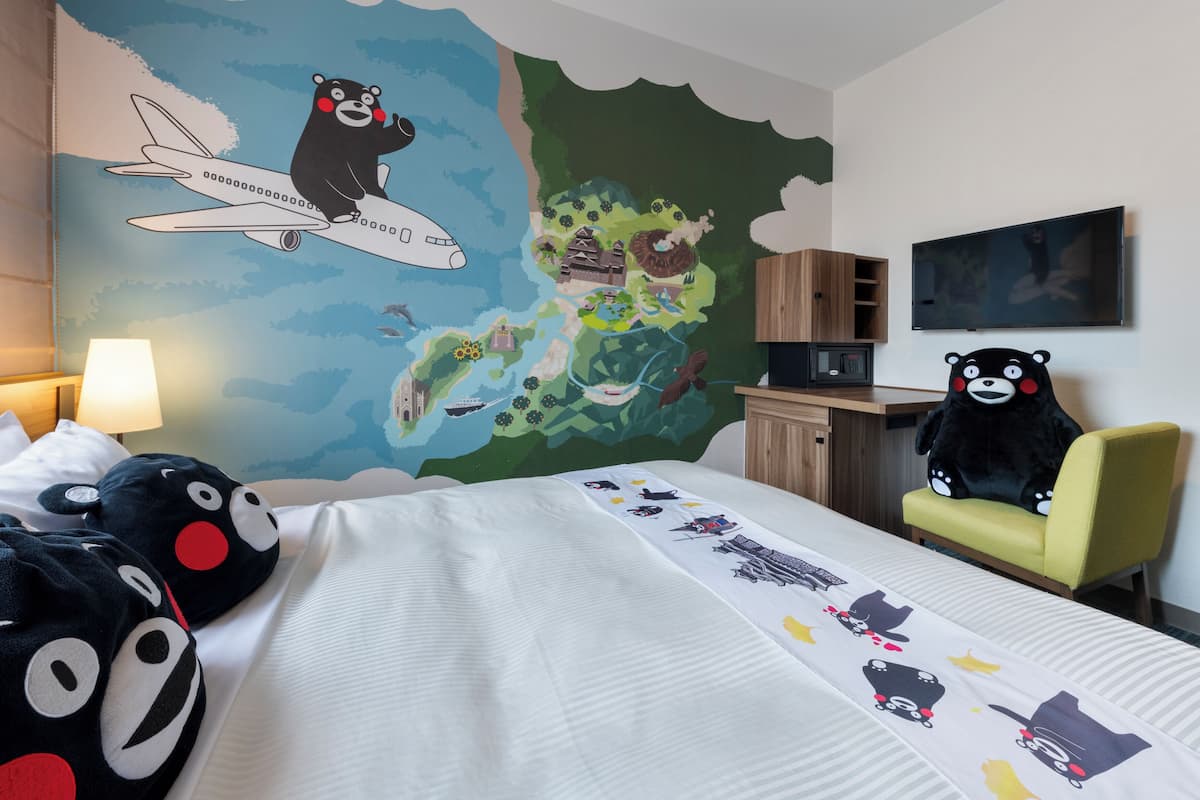 Hotelkamer met een bed, bureau, stoel, pluchen beer en een muurschildering.