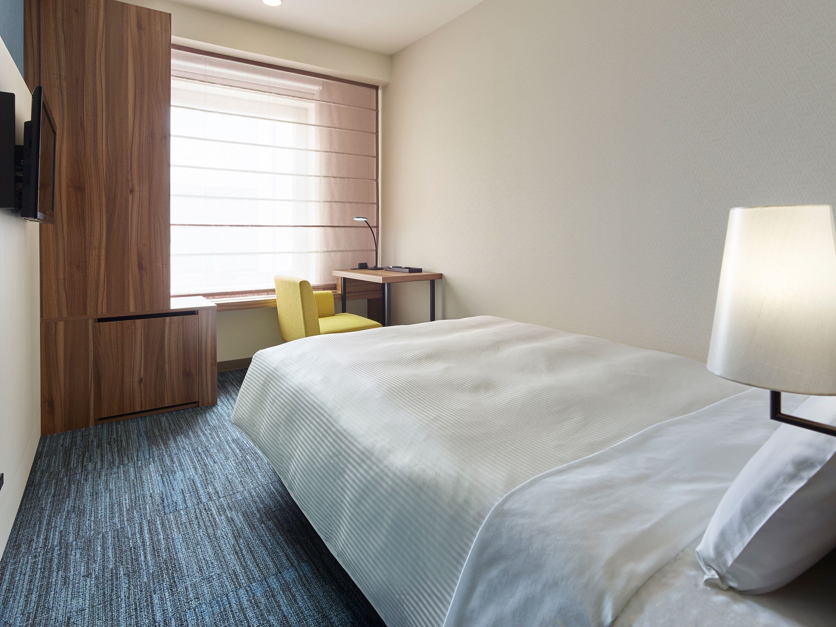 A hotel room with a bed, a desk, a chair, and a window with blinds.