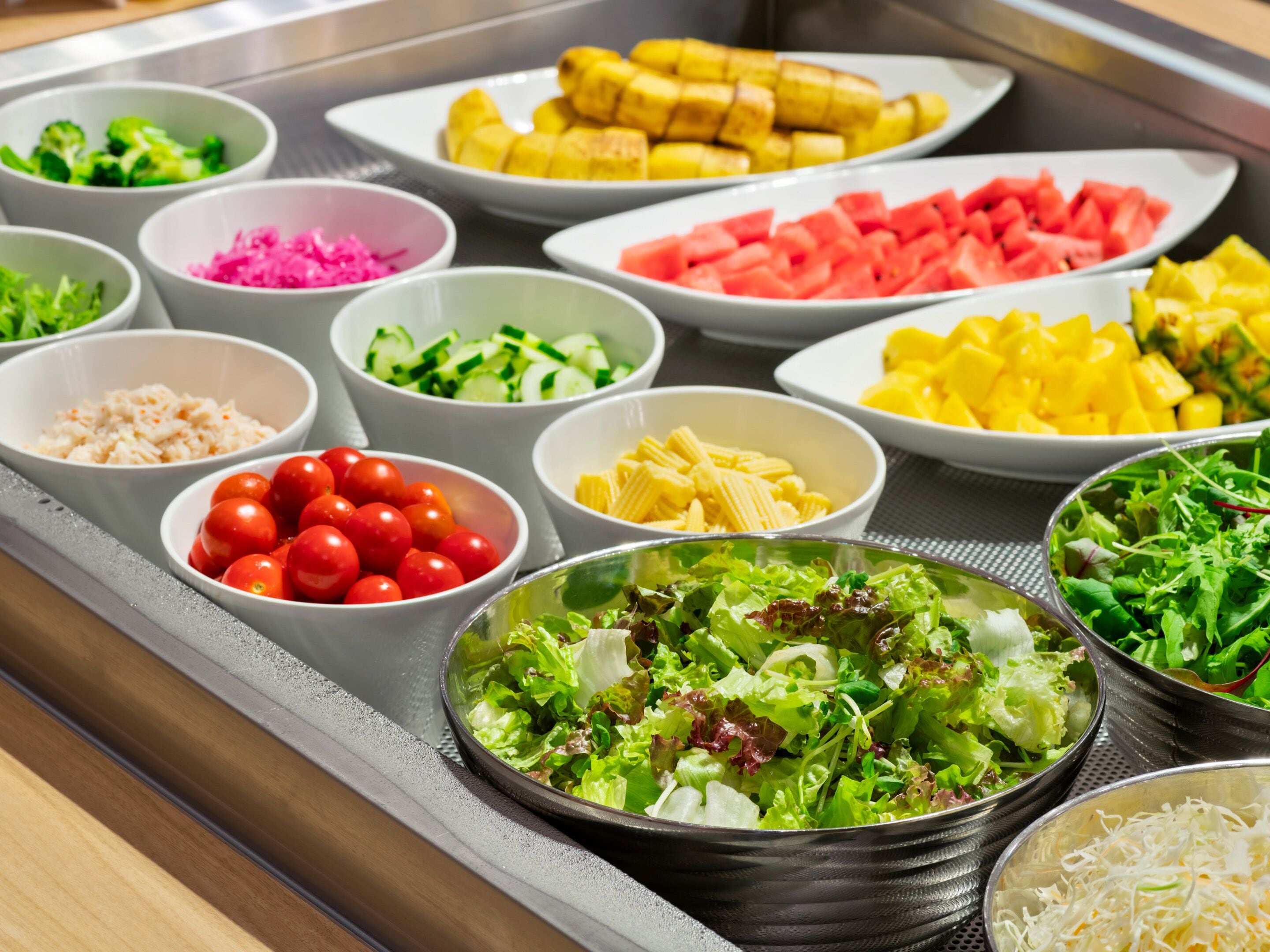 A buffet with various dishes including vegetables, fruits, and salads.