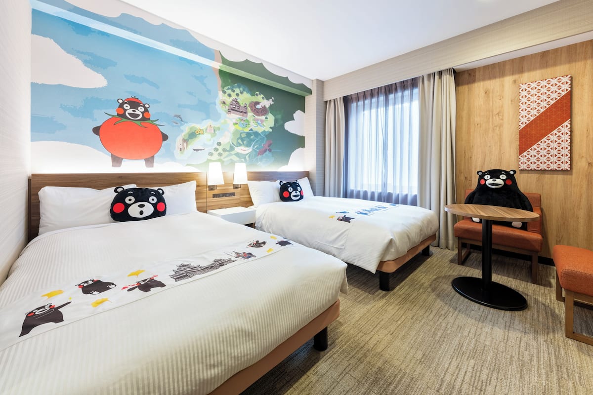 Een hotelkamer met twee bedden, een klein tafeltje en een stoel. Op de muur bevindt zich een muurschildering van een cartoonachtig landschap.