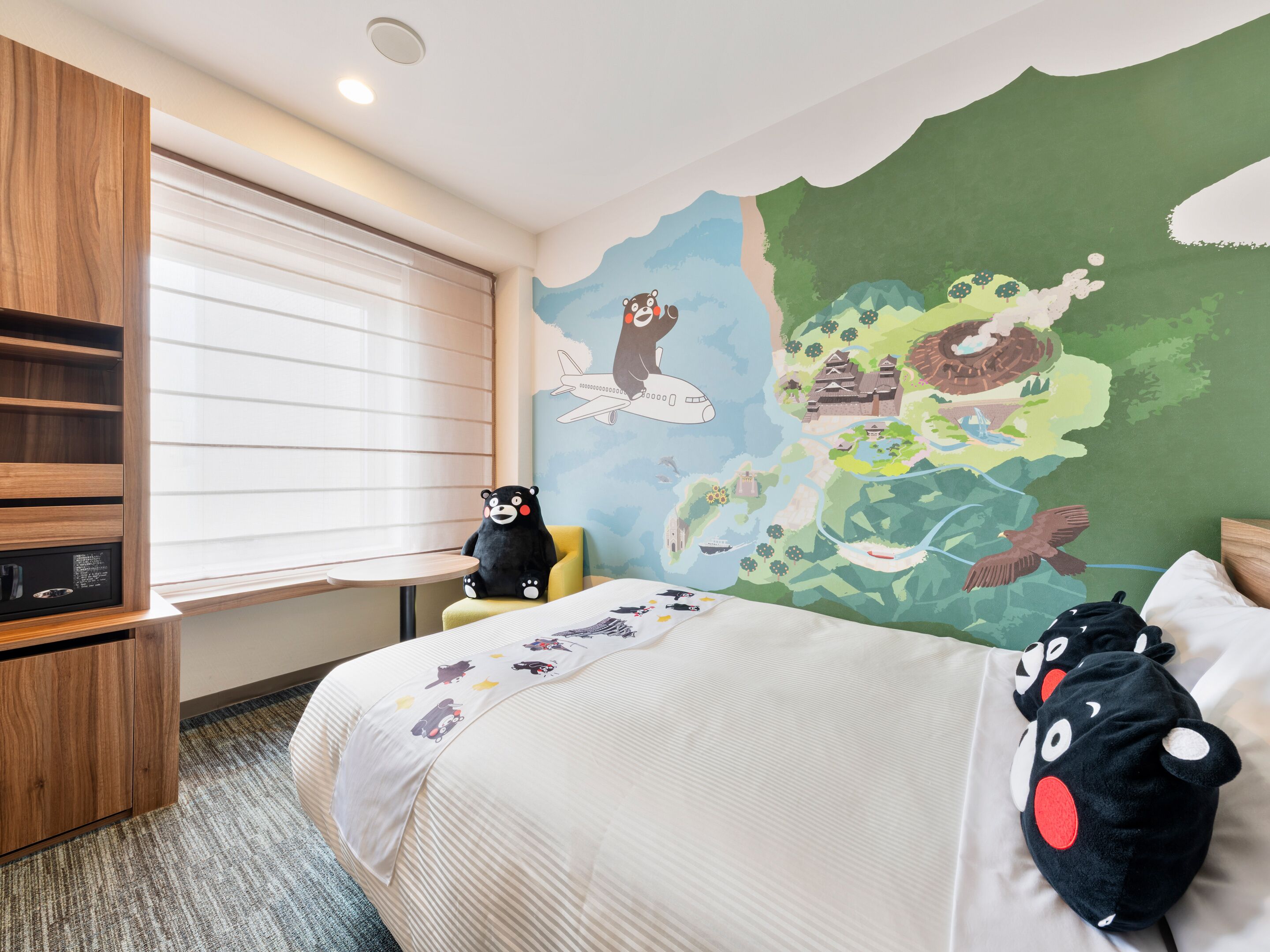 A hotel room with a bed, a small table, a chair, a wooden wardrobe, and a wall with a colorful mural.