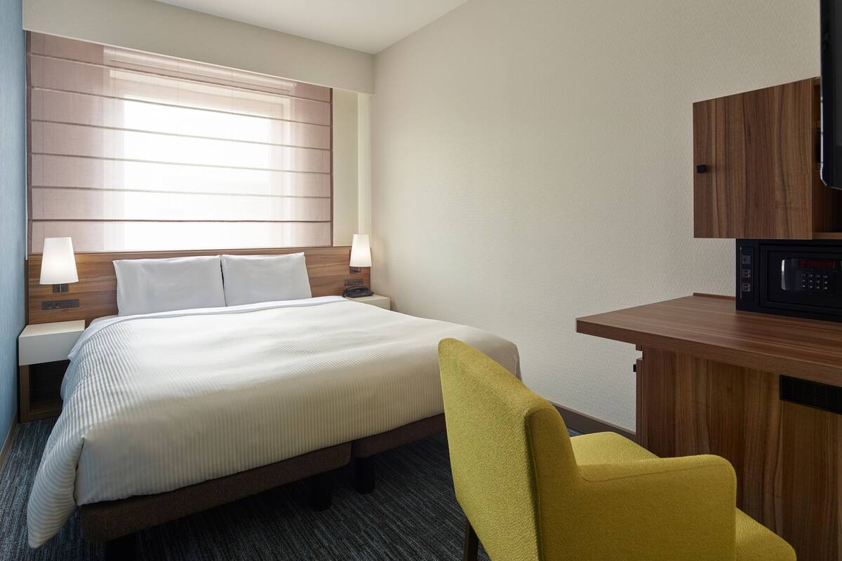 Een hotelkamer met een bed, bedlampen, een bureau, een stoel en een magnetron.