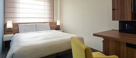 Una habitación de hotel con cama, lámparas de noche, escritorio, silla y microondas.