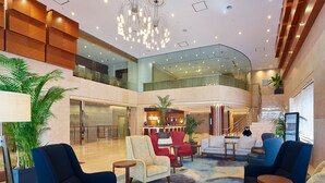 A spacious lobby with a high ceiling, modern furniture, and a central chandelier.