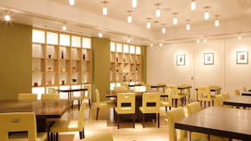 A dining area with yellow chairs and tables, wooden shelves with various items, and ceiling lights.