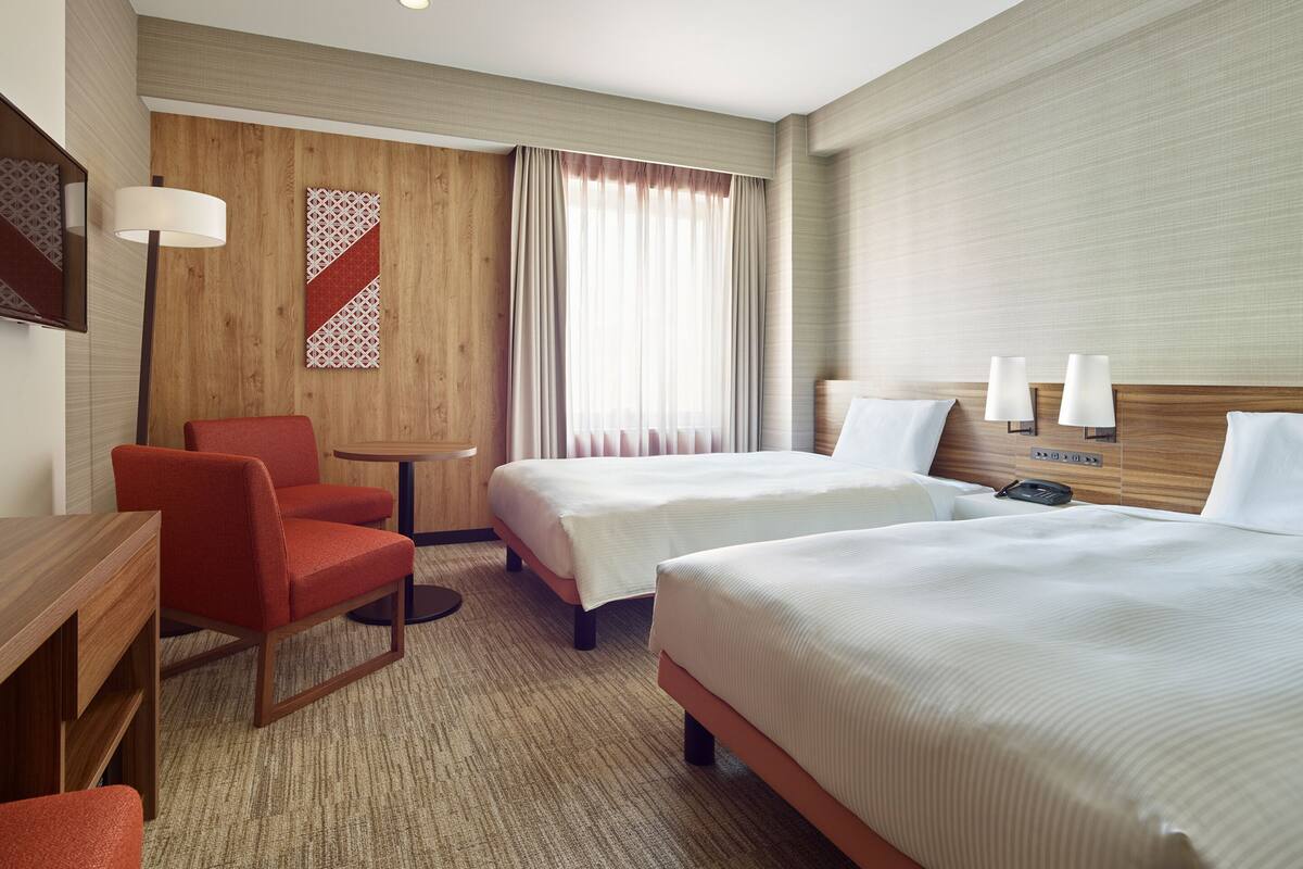 Een hotelkamer met twee bedden, een bureau, een stoel en een klein tafeltje.