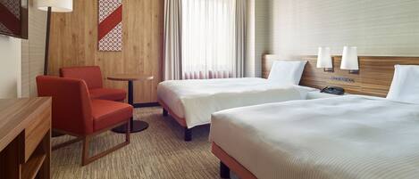 A hotel room with two beds, a desk, a chair, and a small table.