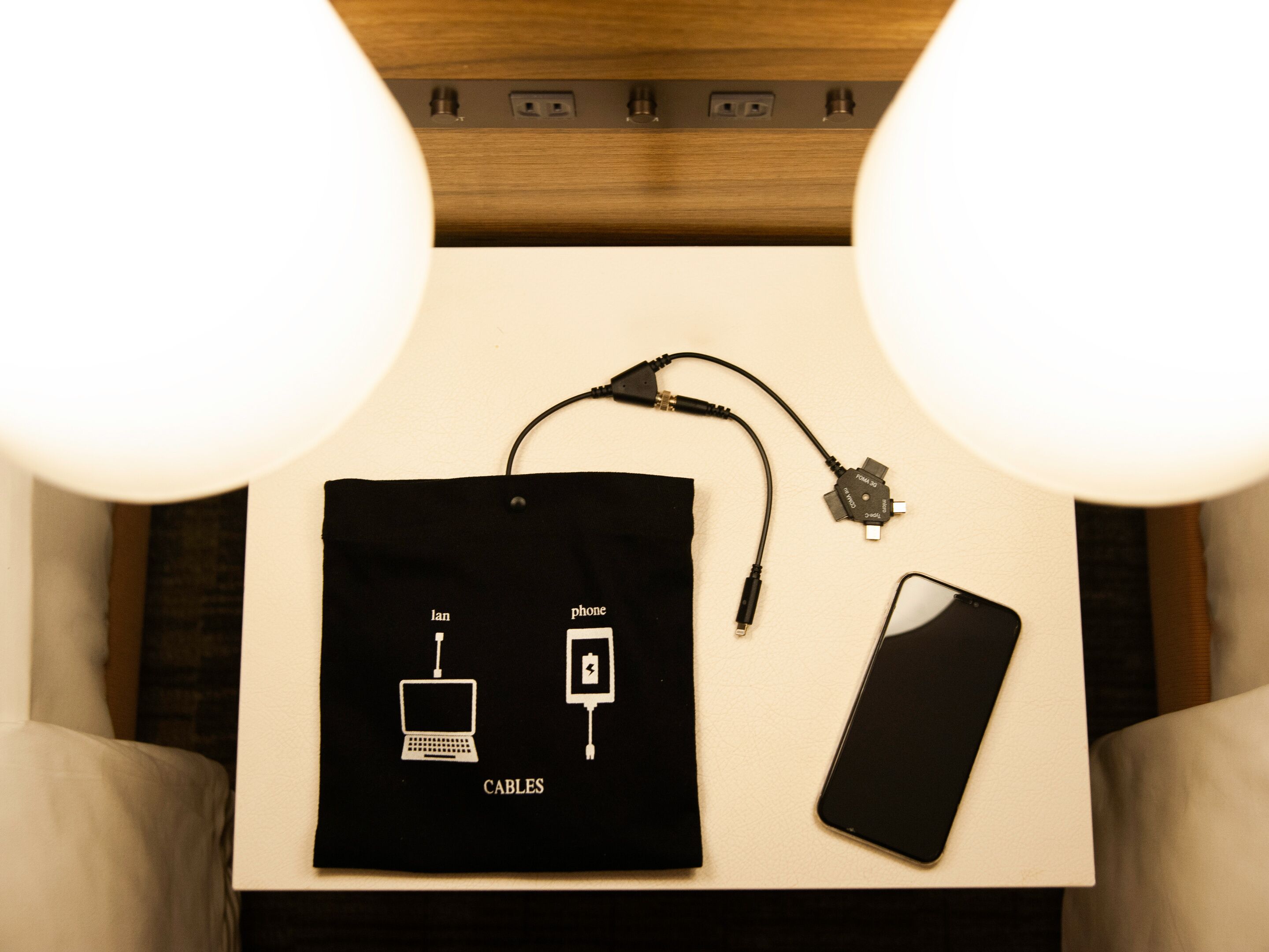 Ein Tisch mit einer schwarzen Tasche mit dem Aufdruck 'CABLES', einem Smartphone und einem USB-Kabel.