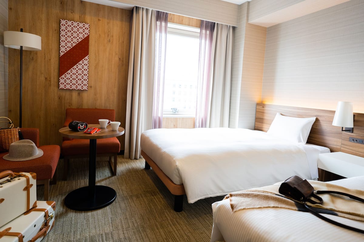 Een hotelkamer met een bed, een bureau met stoel, een tafel met stoel en een lamp.