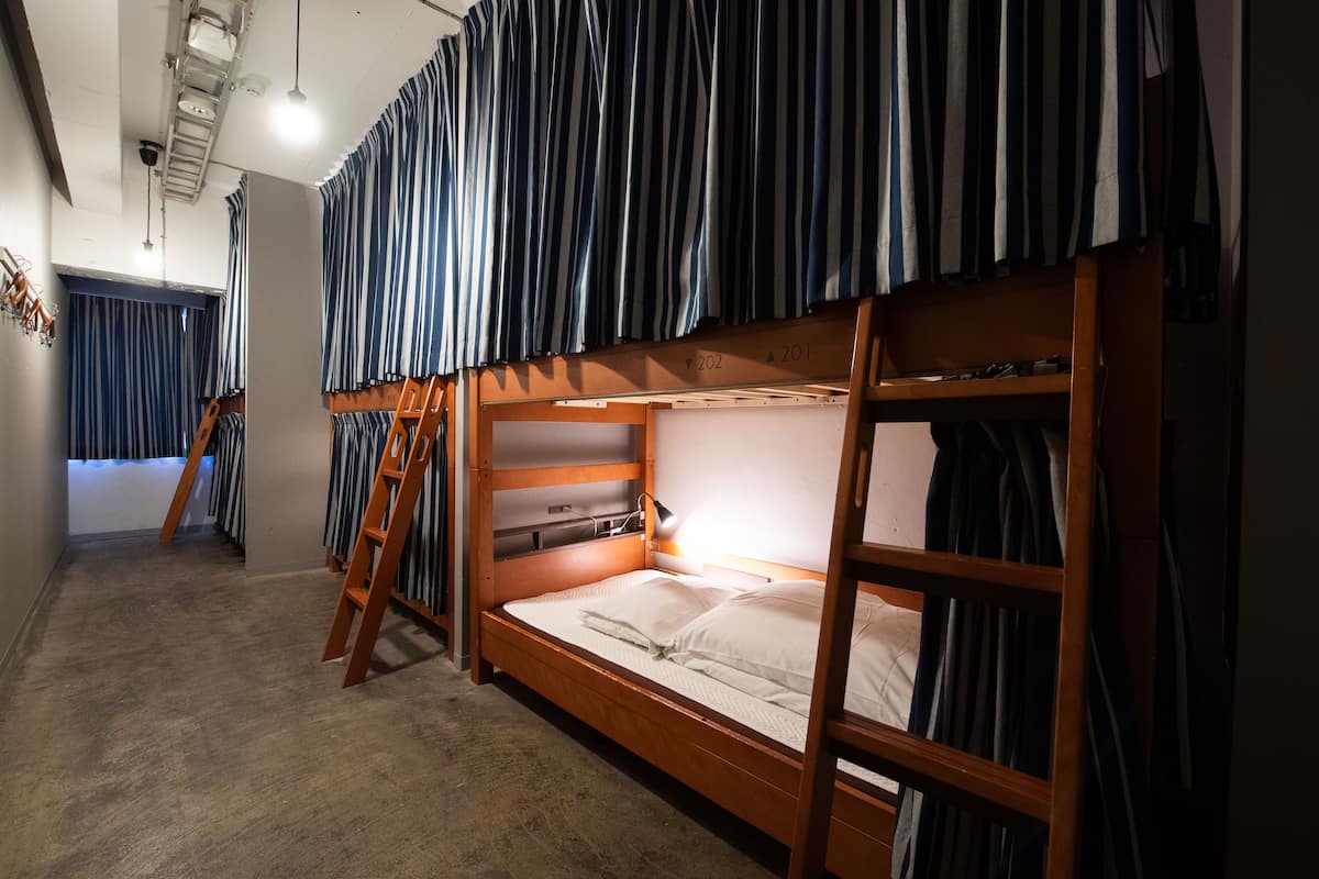 A bunk bed room with striped curtains, a ladder, and a desk with a lamp.