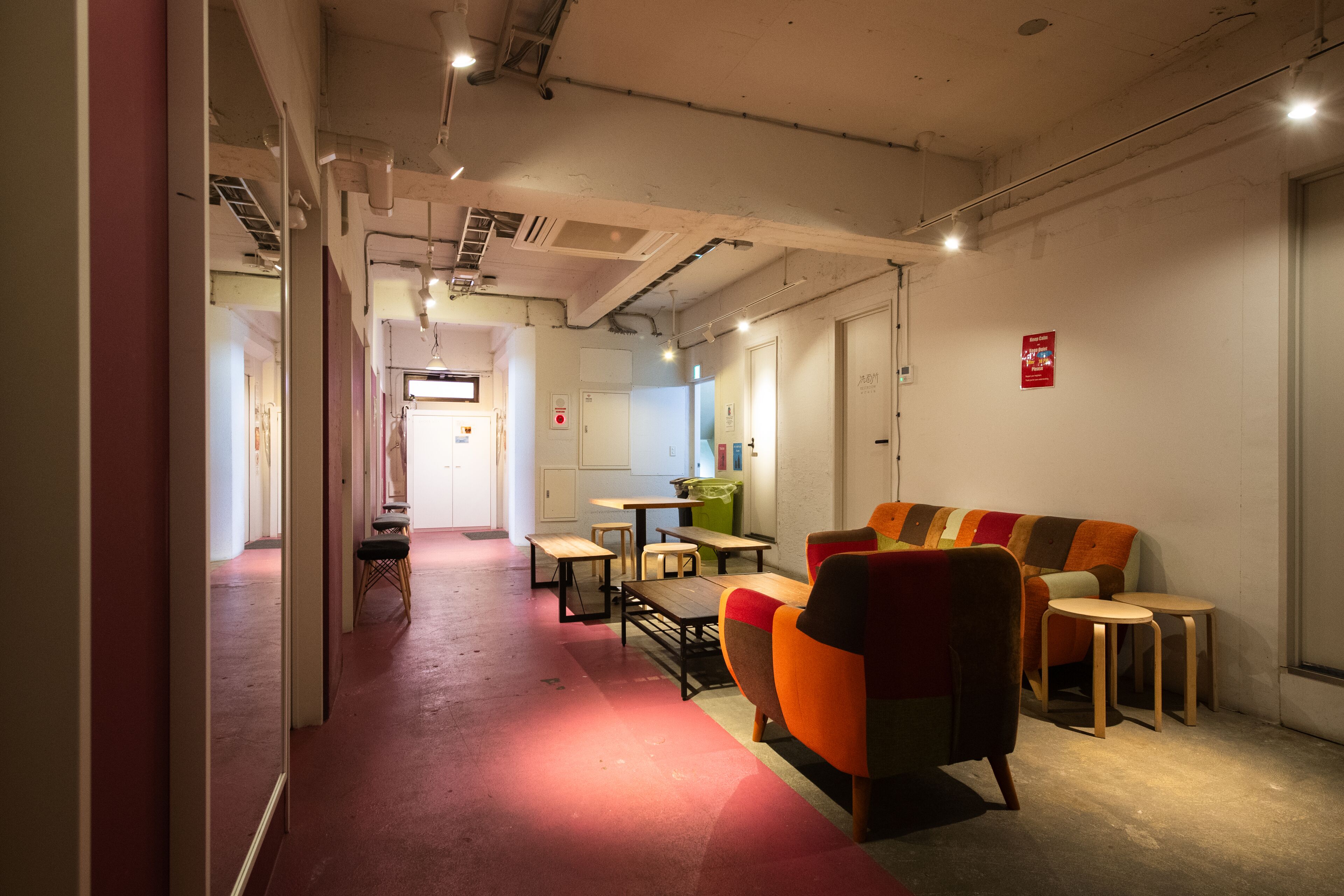 A modern interior with a red carpeted hallway, a colorful sofa, and a small dining area with tables and chairs.