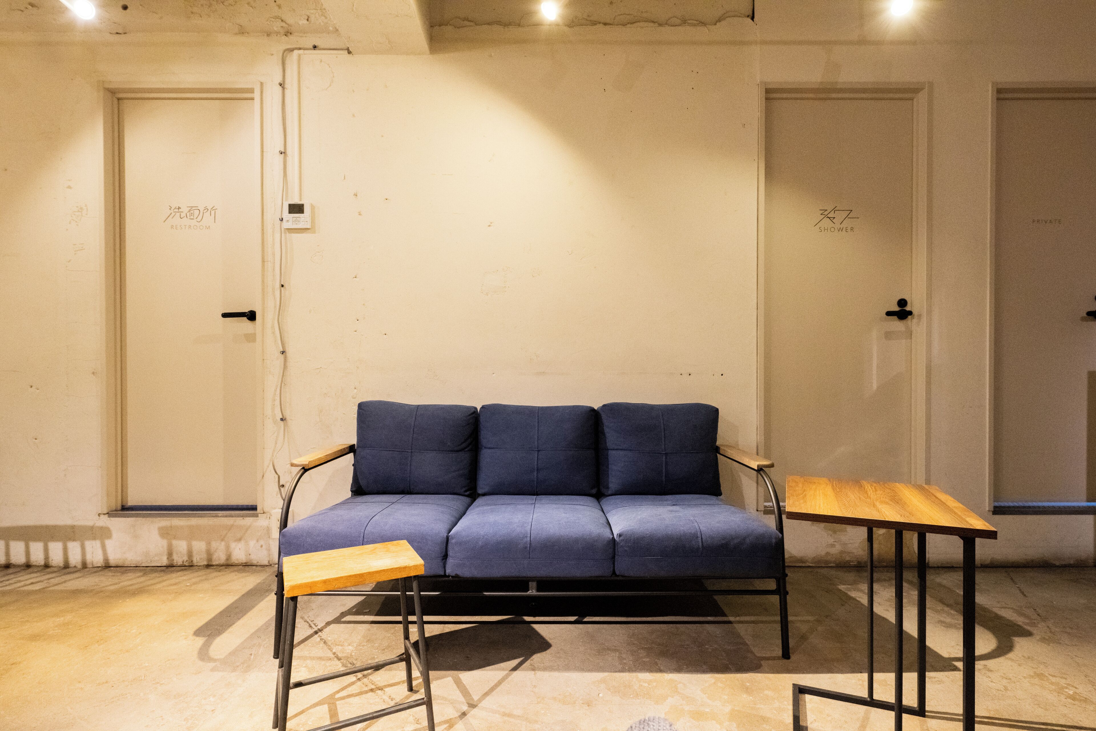 A room with a blue sofa, a wooden table, and two doors labeled "Shower" and "Private."