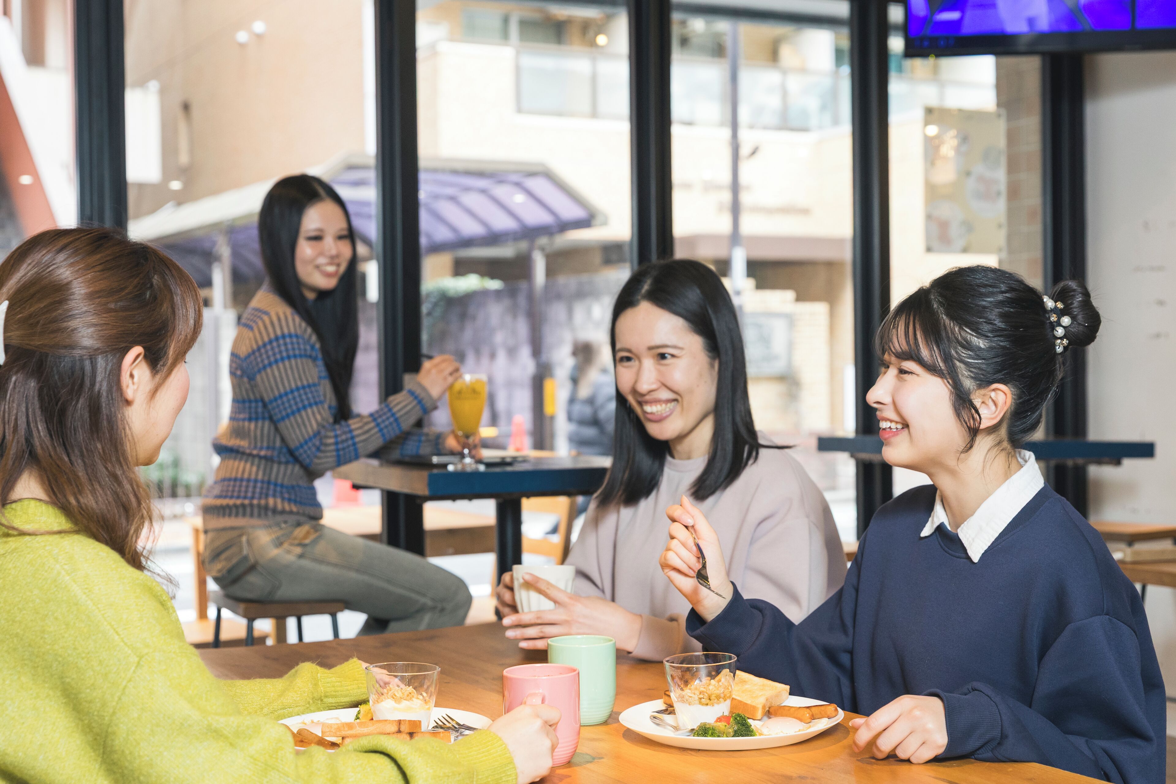 A group of people sitting at a table in a cafe with a view of the street outside.