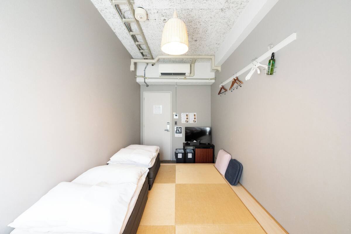 A compact hotel room with a bed, a small desk, a television, and a shelf with personal items.