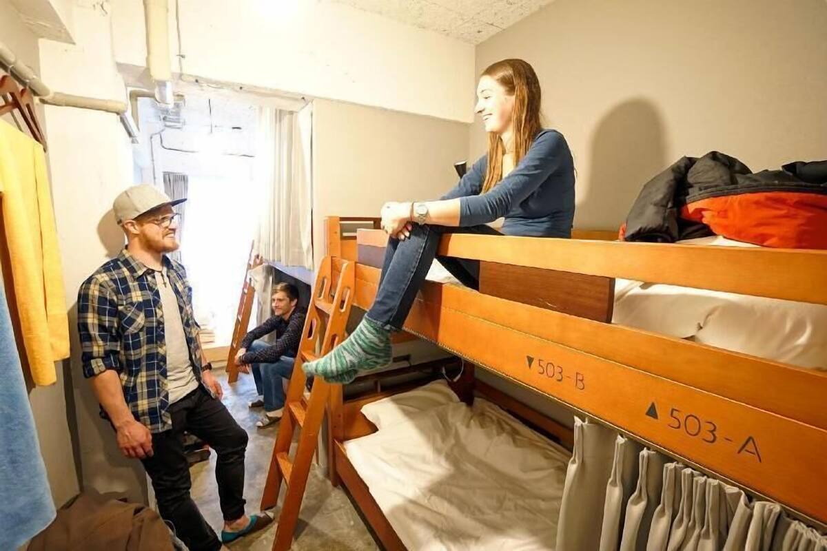 A dormitory room with bunk beds, a wooden ladder, and a visible door.