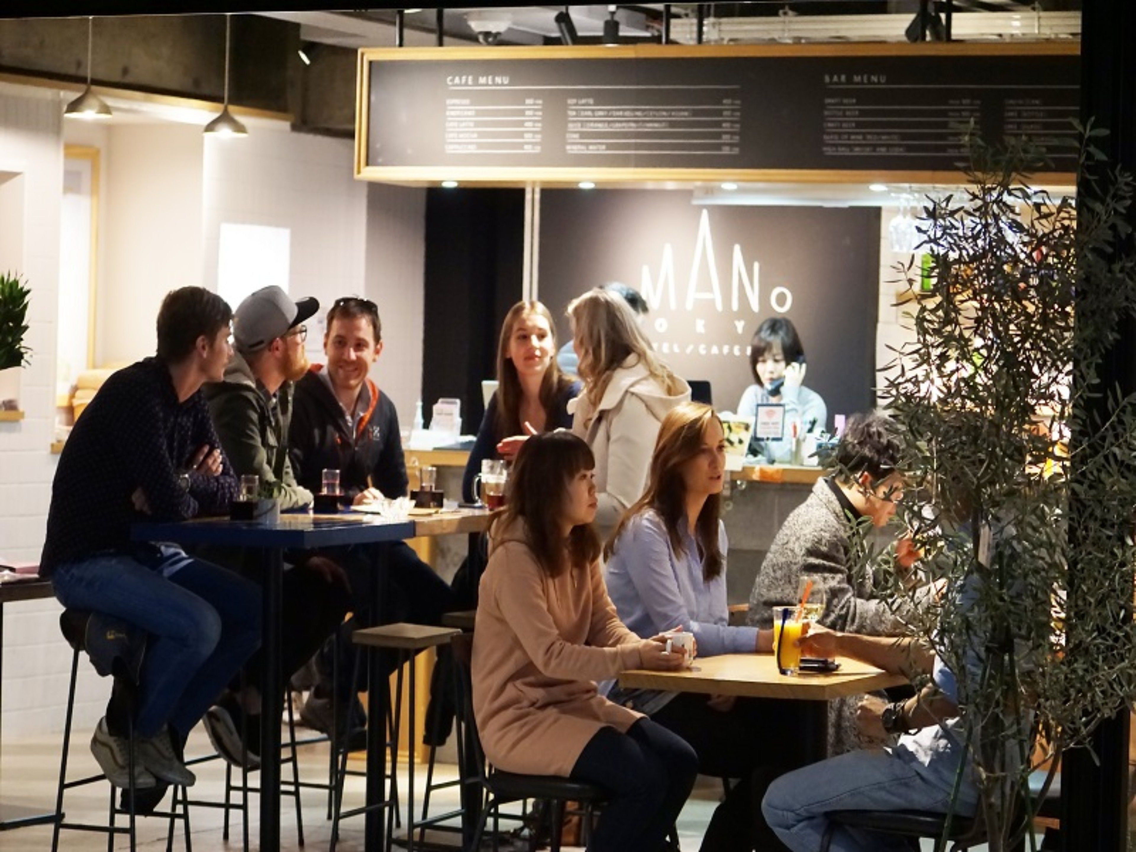 A group of people seated at tables in a cafe with a menu board in the background.