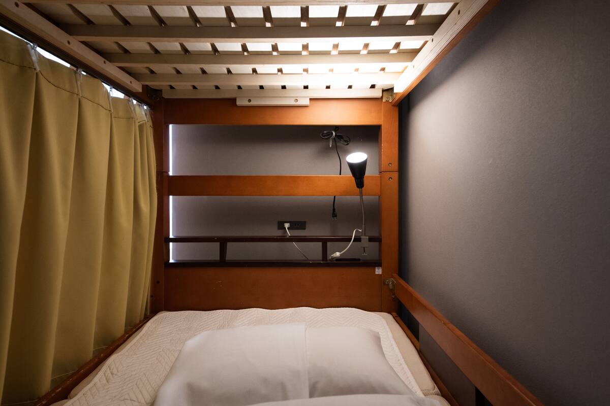 A compact room with a bed, a ceiling fan, and a window with curtains.