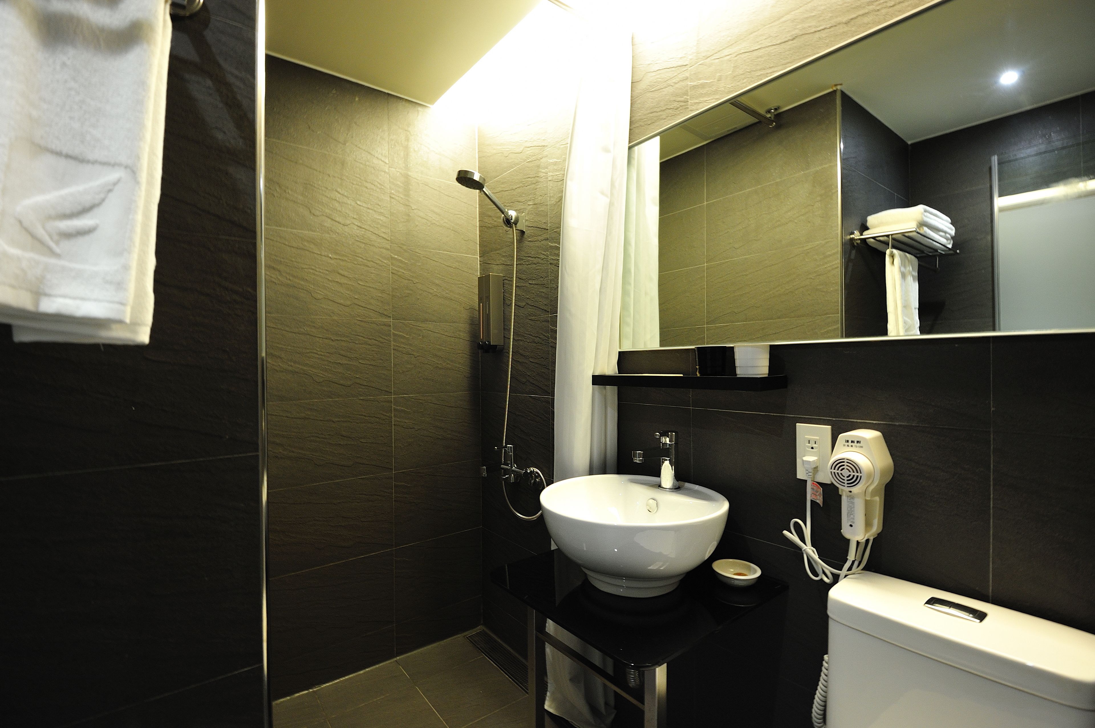 Une salle de bain moderne dotée d’un grand lavabo, d’une douchette à main, d’un porte-serviettes et d’un sèche-cheveux.