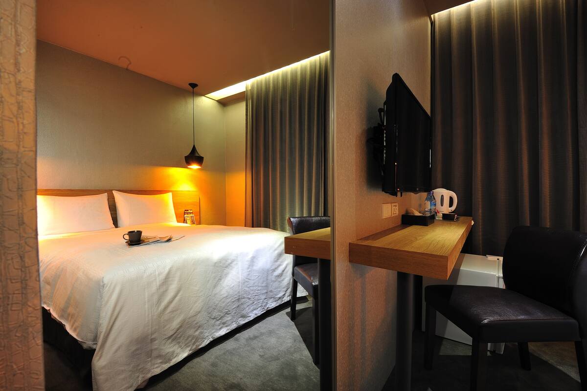 Una habitación de hotel con cama, mesita de noche, silla y televisor.