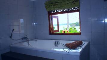 A bathroom with a large bathtub, a window with a view of greenery, and a towel rack with a towel.