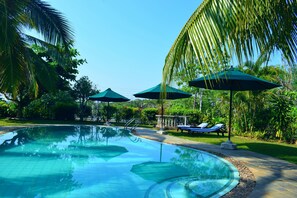 A swimming pool with lounge chairs and umbrellas, surrounded by lush greenery. - Asian Jewel Boutique Hotel (Hikkaduwa)