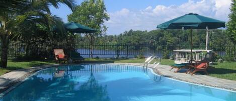 A swimming pool with lounge chairs and umbrellas, surrounded by palm trees and a fence.