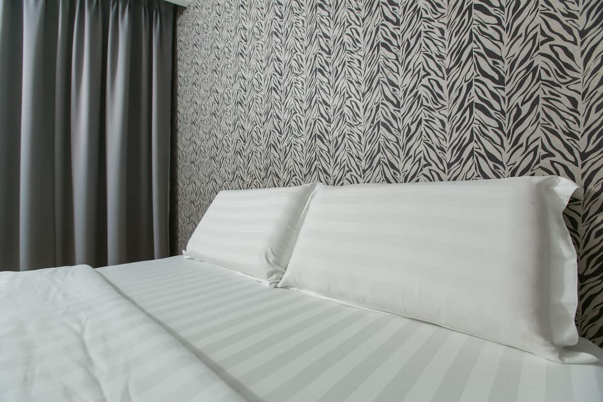 Un lit avec une literie blanche et un mur à motifs zébrés derrière.