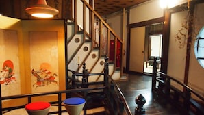 A traditional Japanese interior with tatami flooring, a wooden staircase, and a low table with a red cushion.