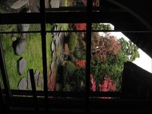 A view through a window with a stone wall, a grassy area, and trees with red foliage. - Ishiba Ryokan (Hirosaki)