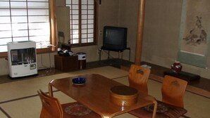 A traditional Japanese-style room with tatami flooring, a low table with cushions, and a television in the background.