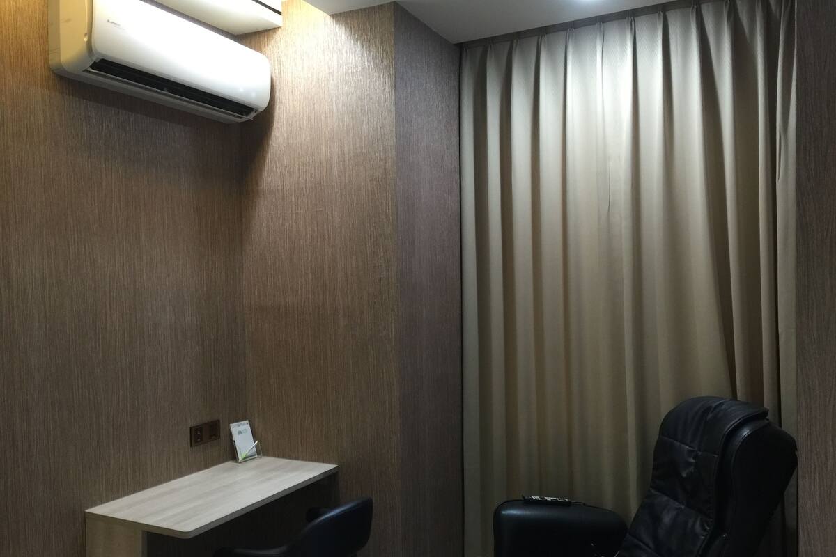 Habitació amb escriptori, dues cadires, una cadira de pell negra, aire condicionat i una cortina.
